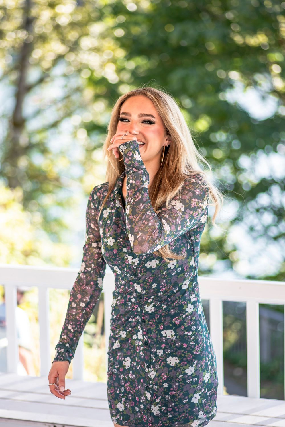 Woman in floral dress singing with microphone on outdoor wooden deck.