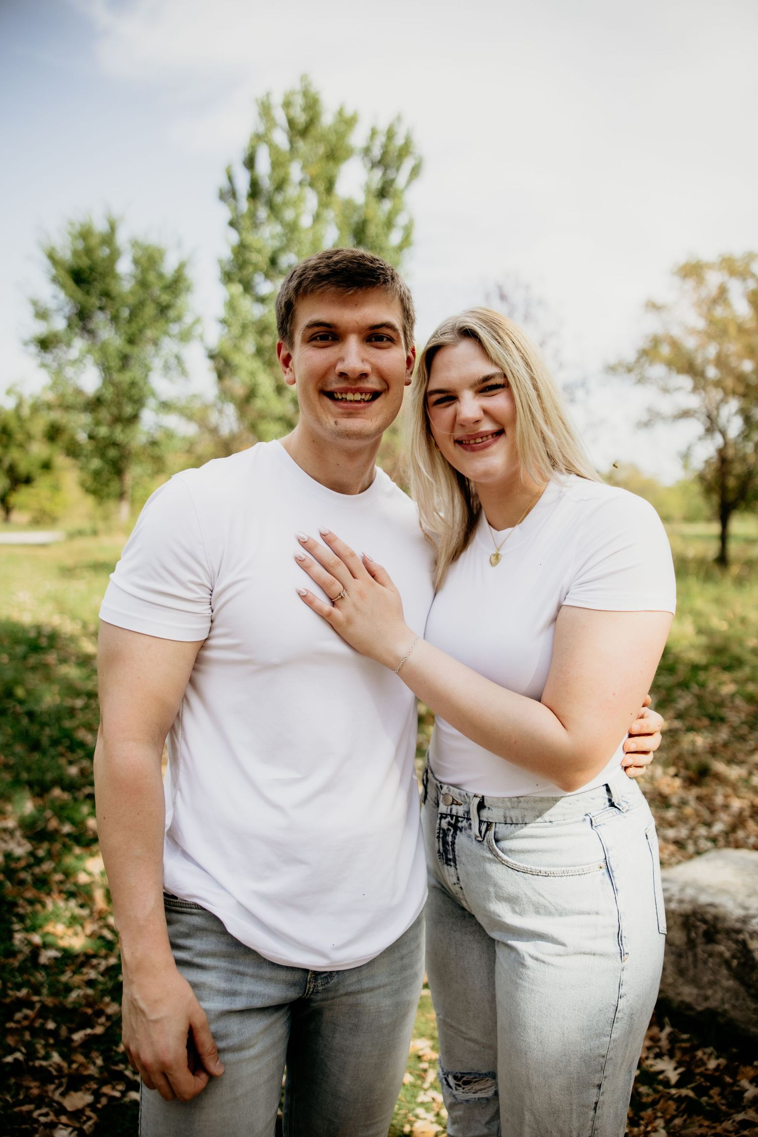 Couple in matching white t-shirts pose together outdoors during engagement photoshoot.