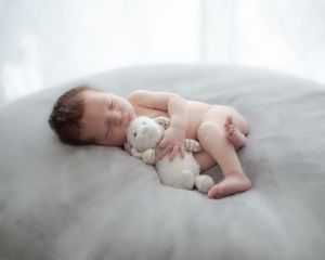 Sleeping infant cuddling small stuffed animal on gray cushion.