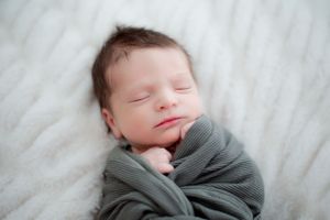 Newborn baby wrapped in gray swaddle blanket during peaceful slumber.