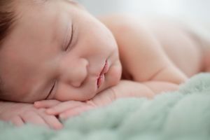Peaceful sleeping newborn baby resting on soft mint green blanket.