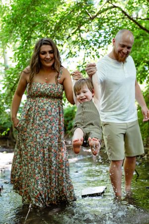 A family plays together in a creek on a sunny summer day surrounded by green trees.