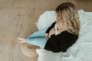 Woman in black sweater relaxing on white bedding while sitting on concrete floor.