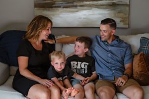 Family relaxing together on grey couch with matching t-shirts in living room.