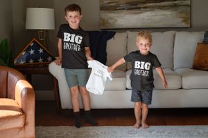 Two children in matching Big Brother shirts jumping on couch.