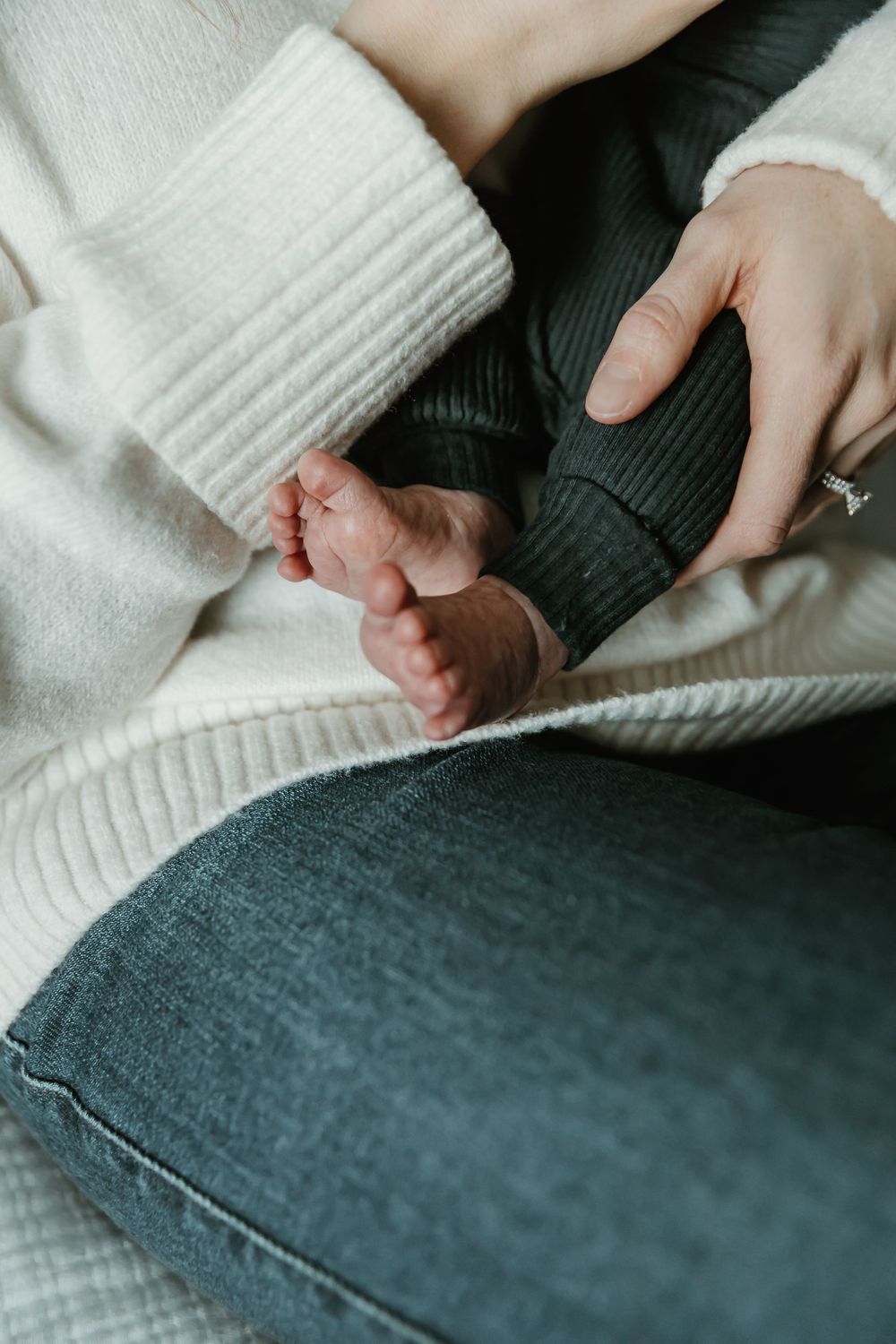 A tiny baby foot being held gently against cozy white knit fabric and dark denim.
