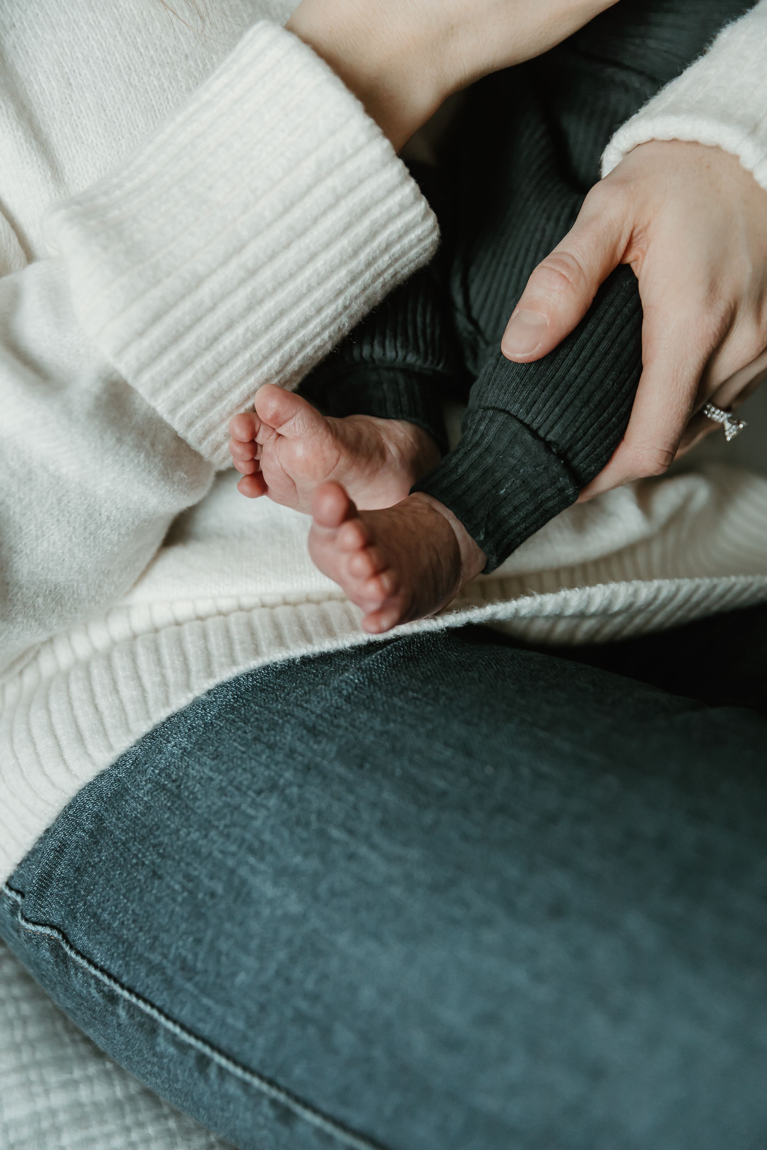 A tiny baby foot being held gently against cozy white knit fabric and dark denim.