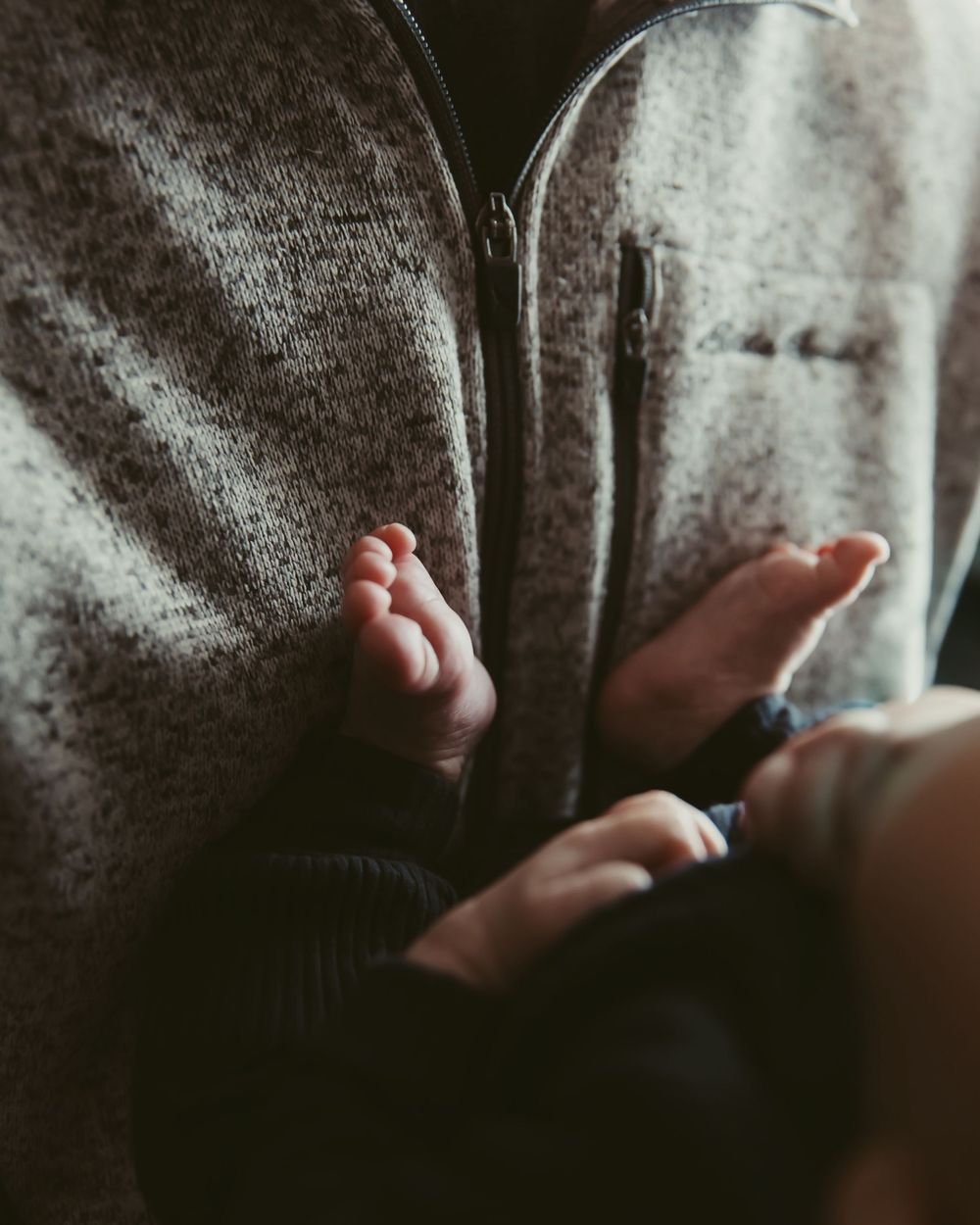 A tiny baby foot rests against a soft gray blanket in an intimate close-up photo.