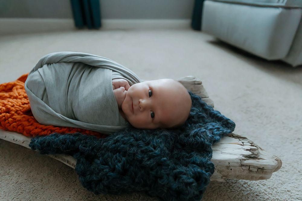 Person lying on plush carpet wearing grey head covering with bright orange and teal textured blankets.