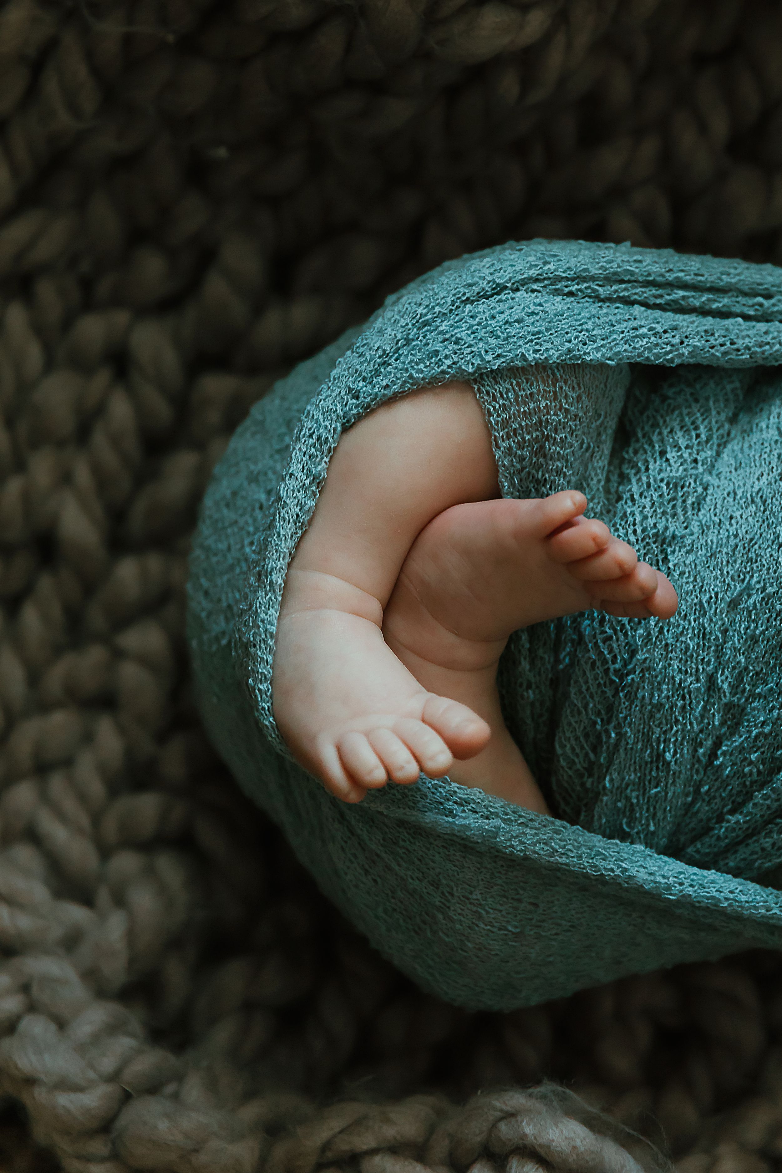 Small baby feet peek out from a soft turquoise blanket against a textured dark background.