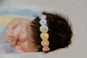 A delicate rainbow-colored button headband adorns dark hair against a soft blurred background.