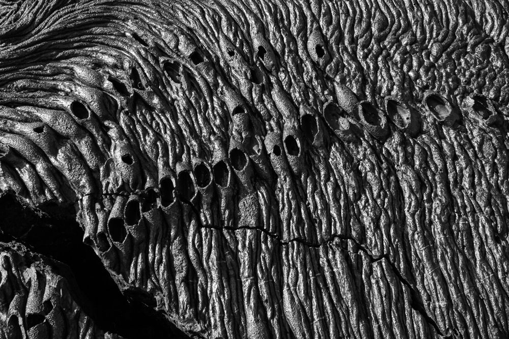 Dramatic black and white photograph of rippled volcanic rock formations.