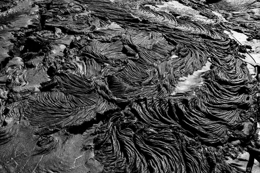 Abstract black and white patterns of volcanic rock formations creating rippled textures.