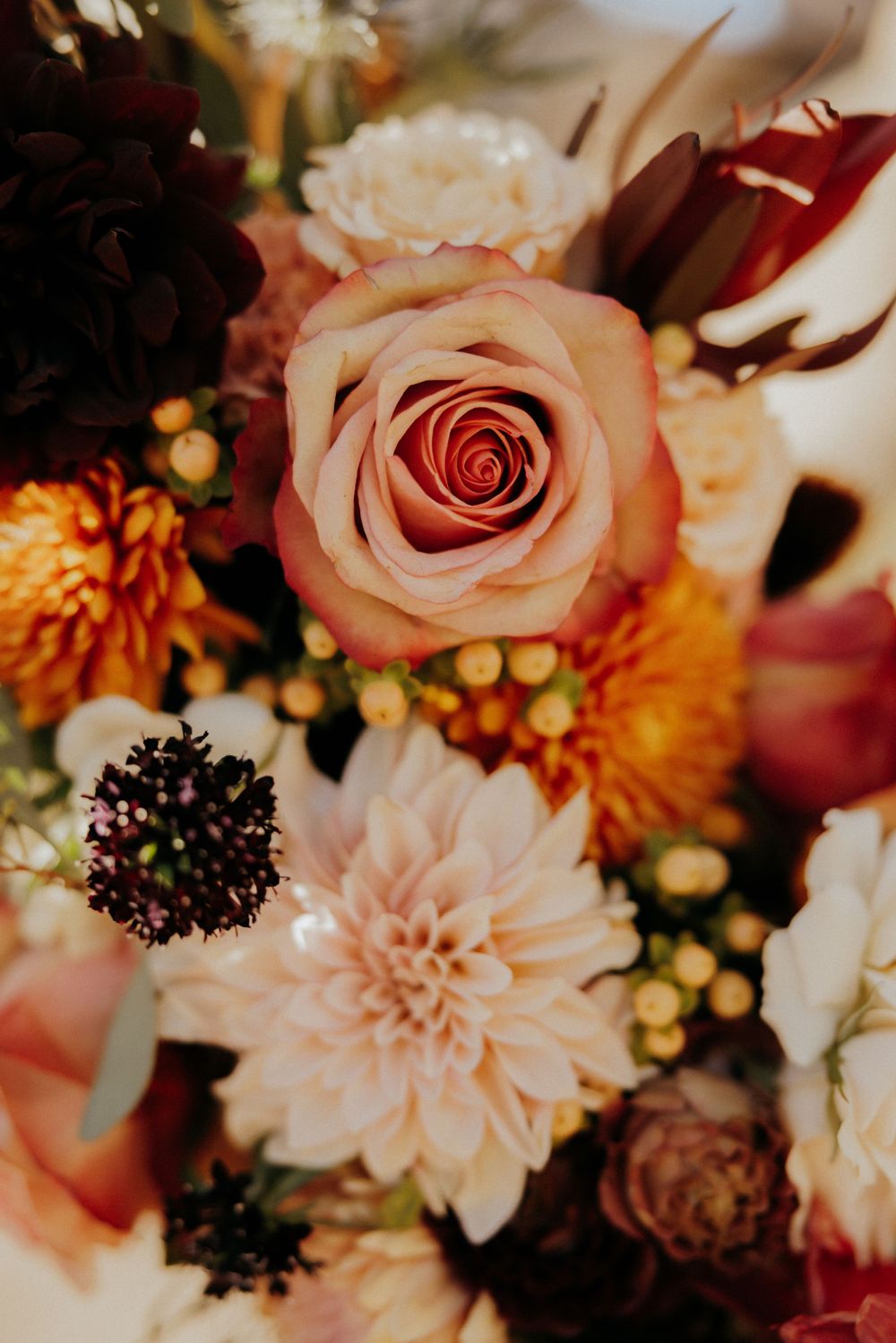 Detailed macro shot of a wedding bouquet with blush roses, orange dahlias, and cream chrysanthemums.