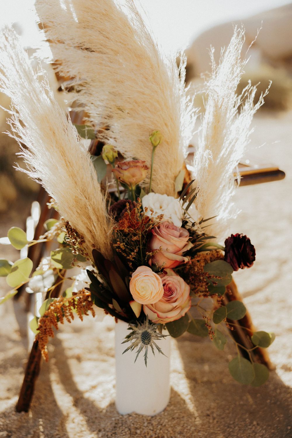 Boho wedding centerpiece with pampas grass, pink roses, and dried flowers in a white vase.