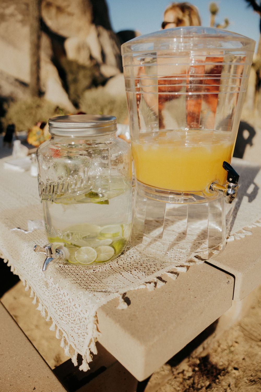Rustic drink station with glass dispensers of refreshing lemonade and cucumber water on burlap cloth.