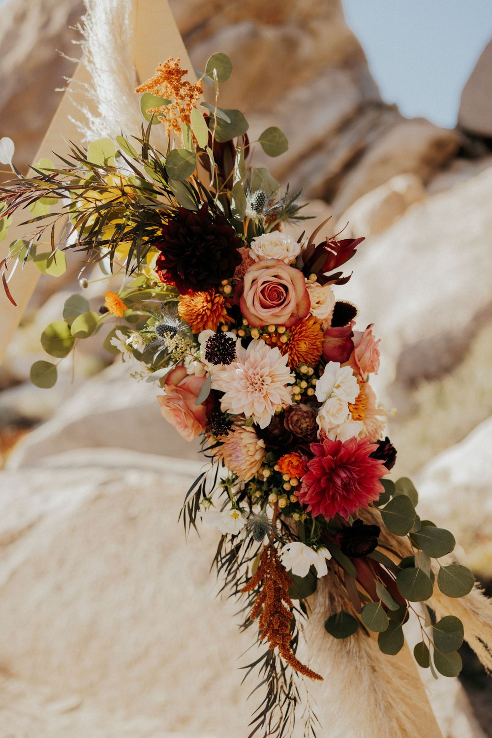 A vibrant autumn-toned wedding bouquet with roses, dahlias, and dried elements.