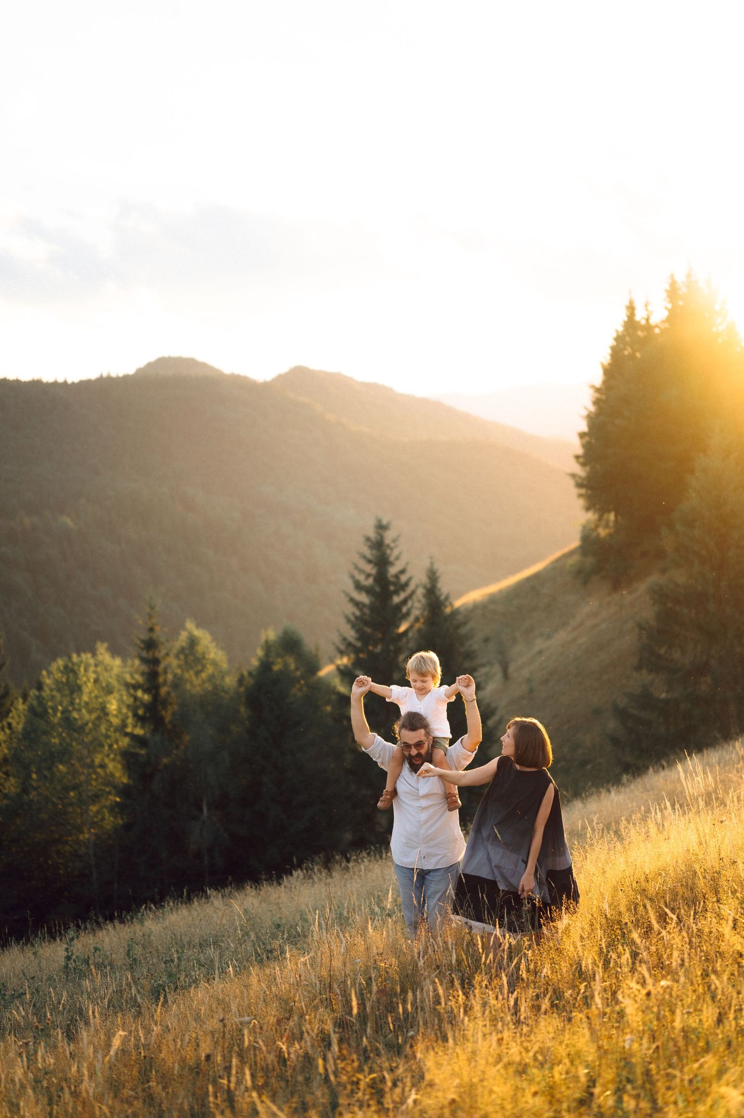 Family walking together on golden hillside during sunset with mountain views.