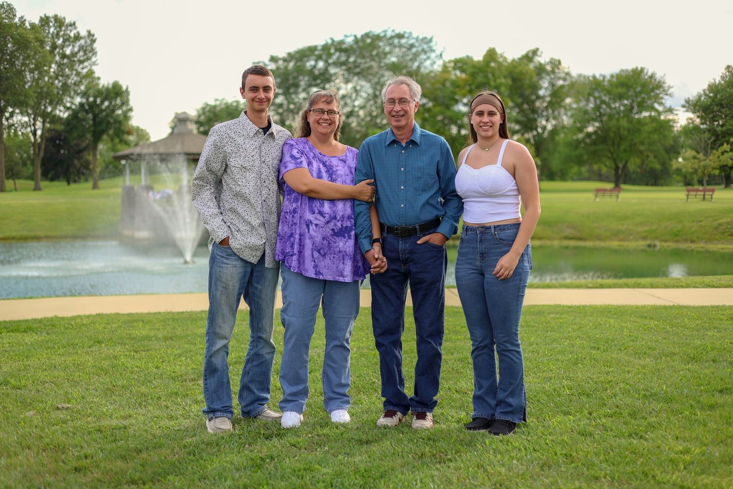 A group stands together on a green lawn with a water feature in the background.
