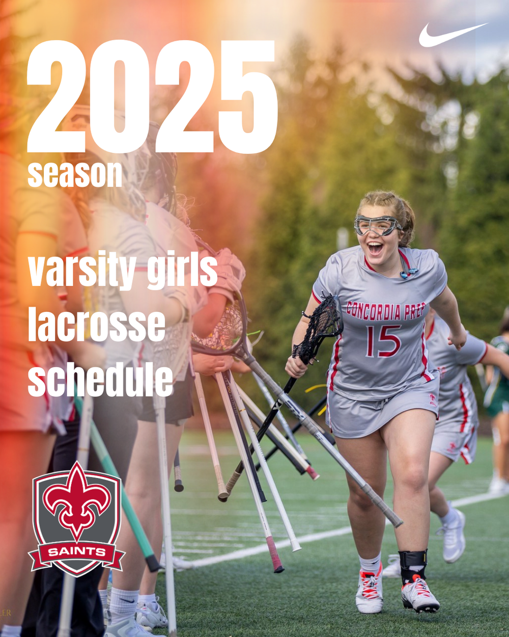 Female lacrosse players in gray jerseys run on a turf field during a sports match at sunset.
