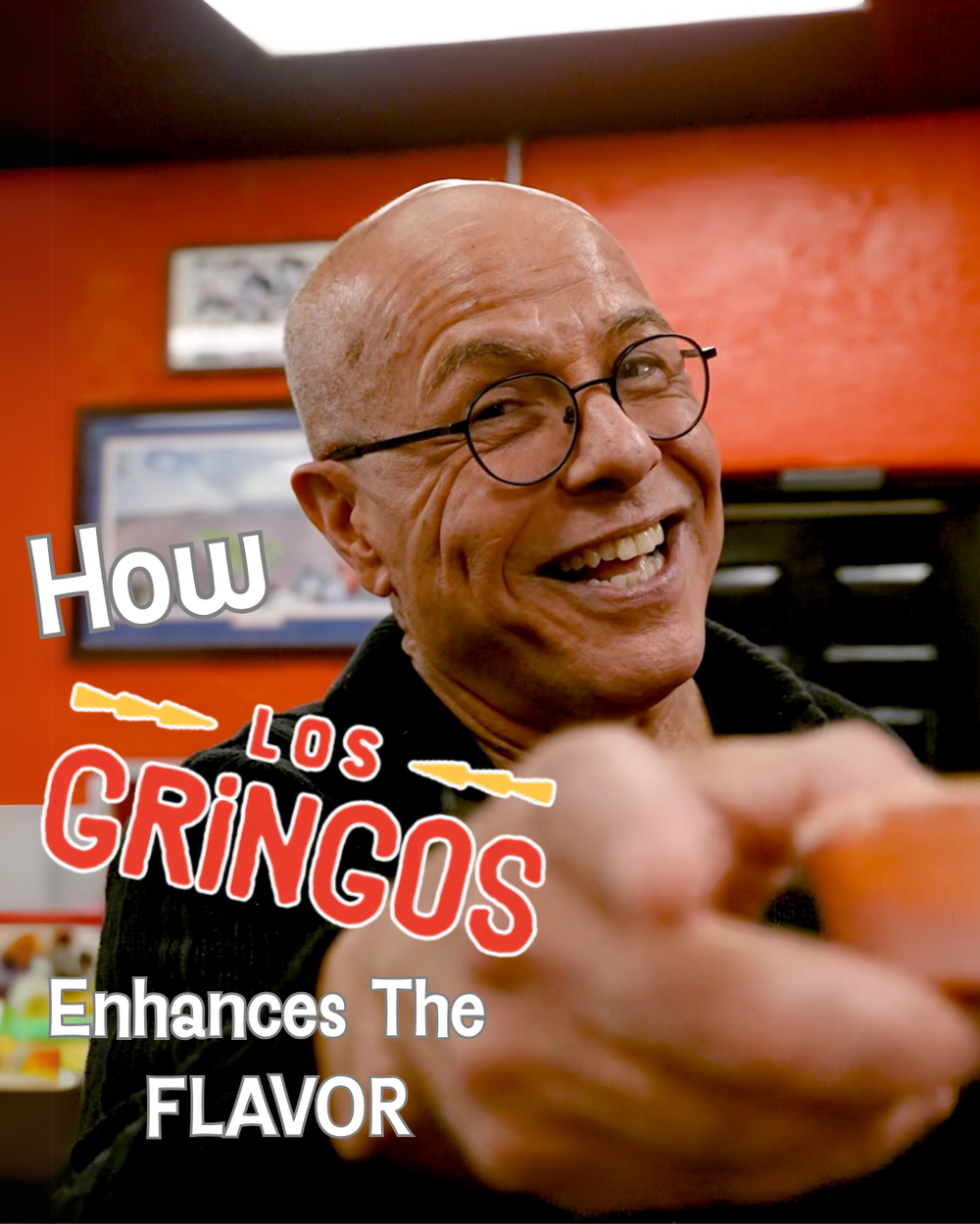Smiling restaurant staff member in glasses shown in warm orange lighting against dark background.