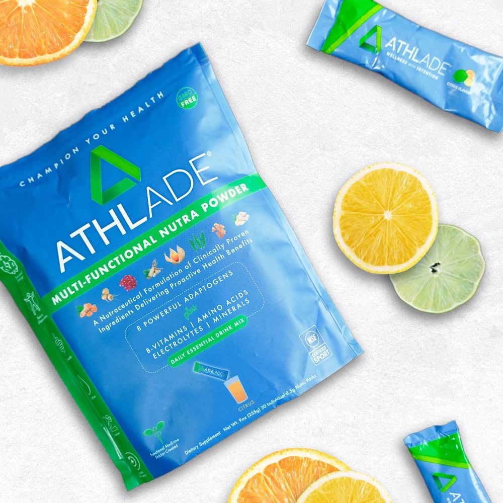 Athlade nutritional supplement packets and citrus fruit slices on white background.