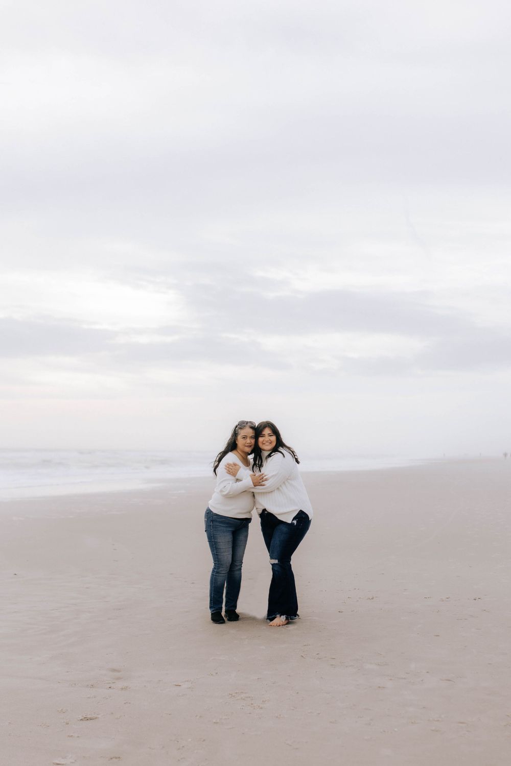People sharing warm moments together on an empty beach under cloudy skies.
