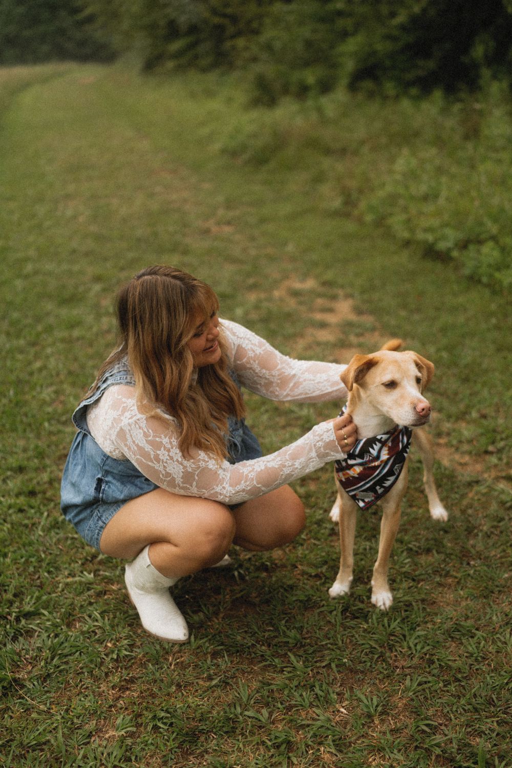 Person in casual attire playing with a tan and white dog on green grass.