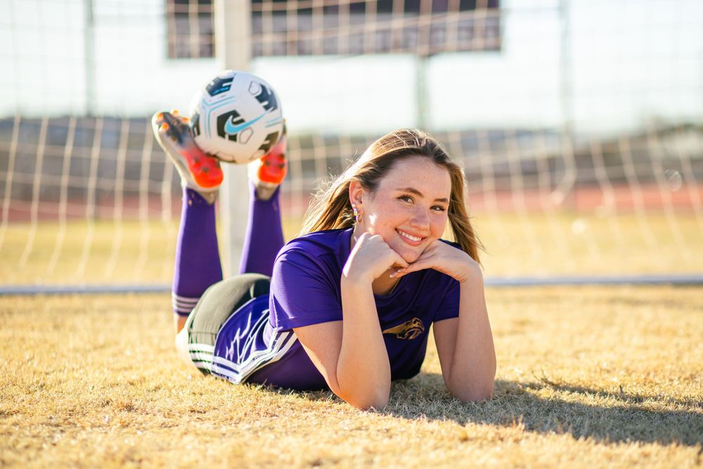 Athletic poses near soccer goal post in purple team uniform.