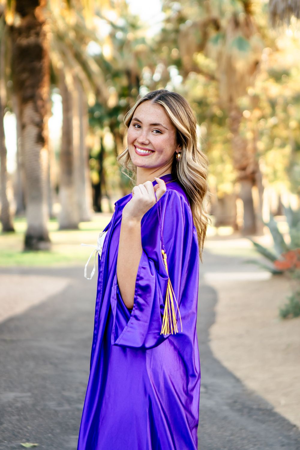 Woman in vibrant purple blouse poses outdoors among trees at sunset.