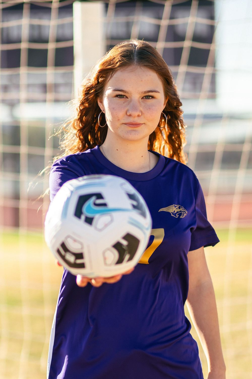 Soccer player in purple jersey holds a white ball during practice.