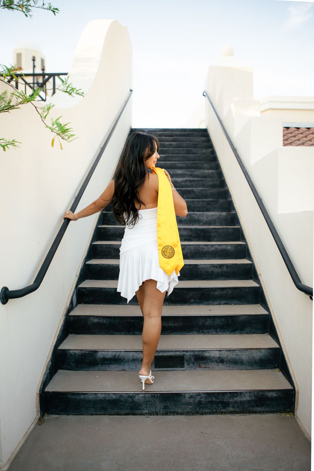 Graduate in yellow stole poses on outdoor staircase.