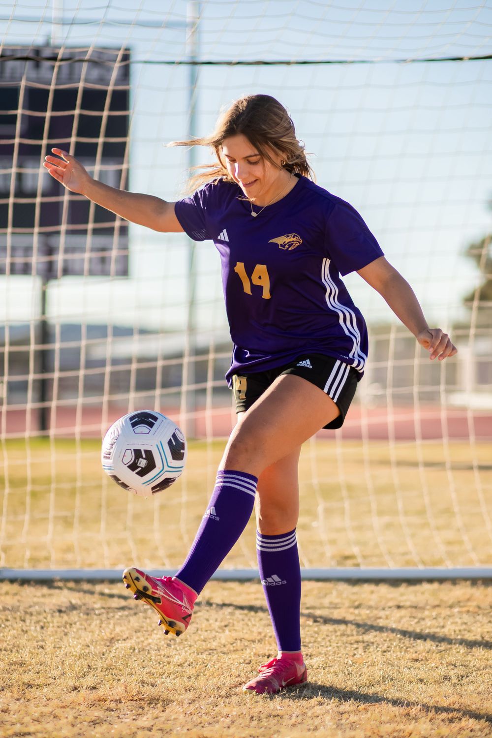 Soccer player in purple uniform practices kicking techniques on a field.