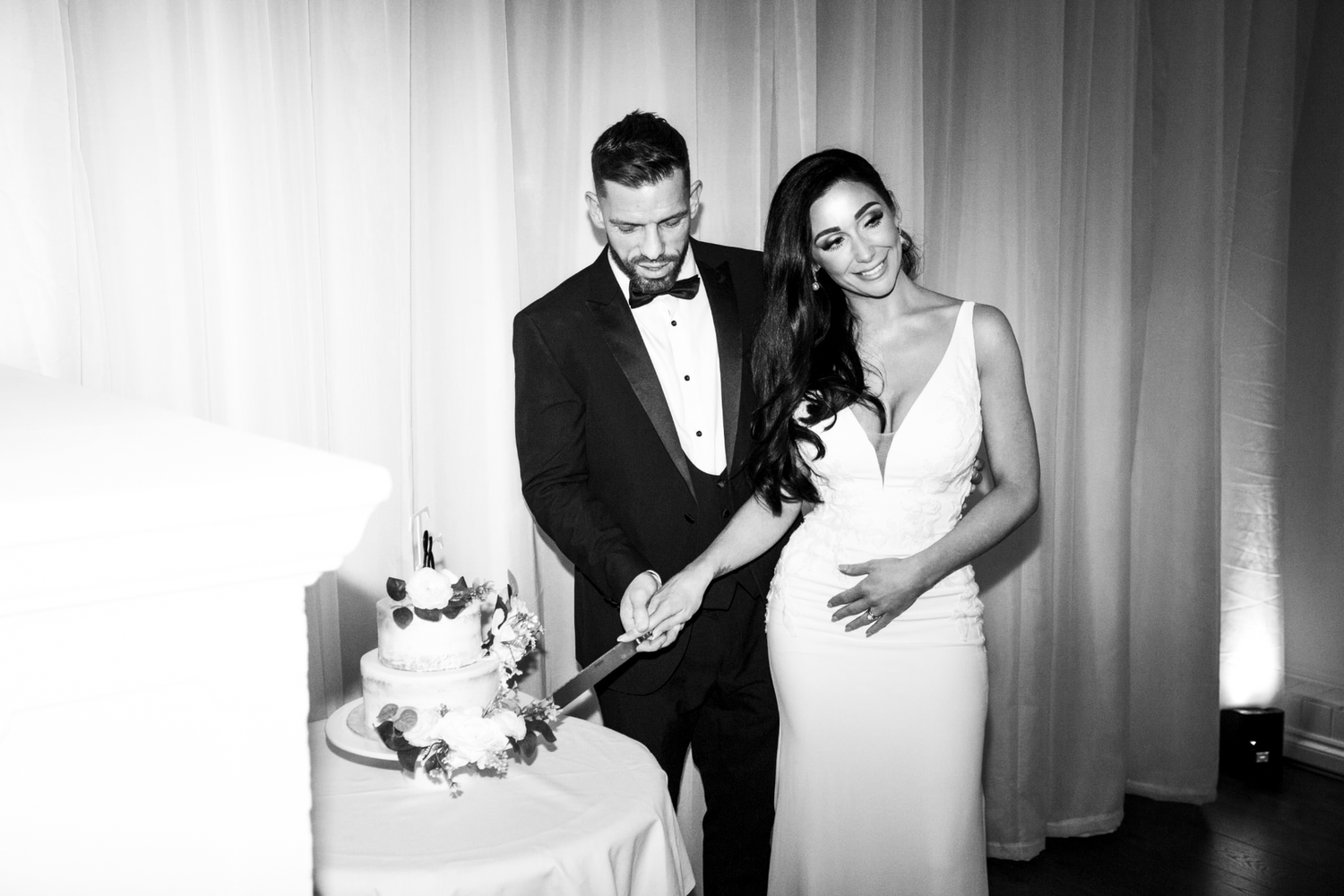 A couple cuts their elegant white wedding cake at an indoor reception.
