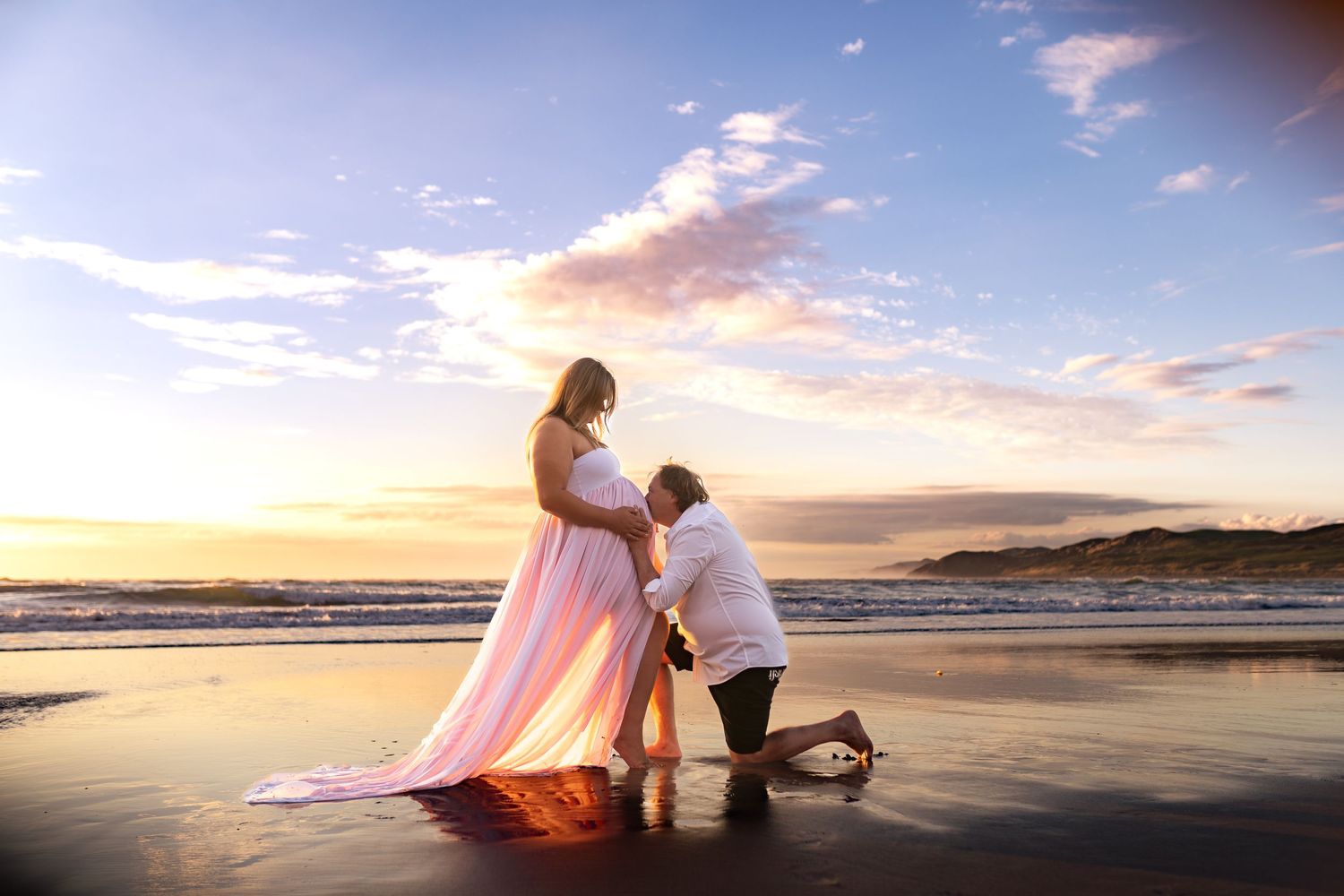 Romantic beach proposal scene at sunset with flowing pink dress.