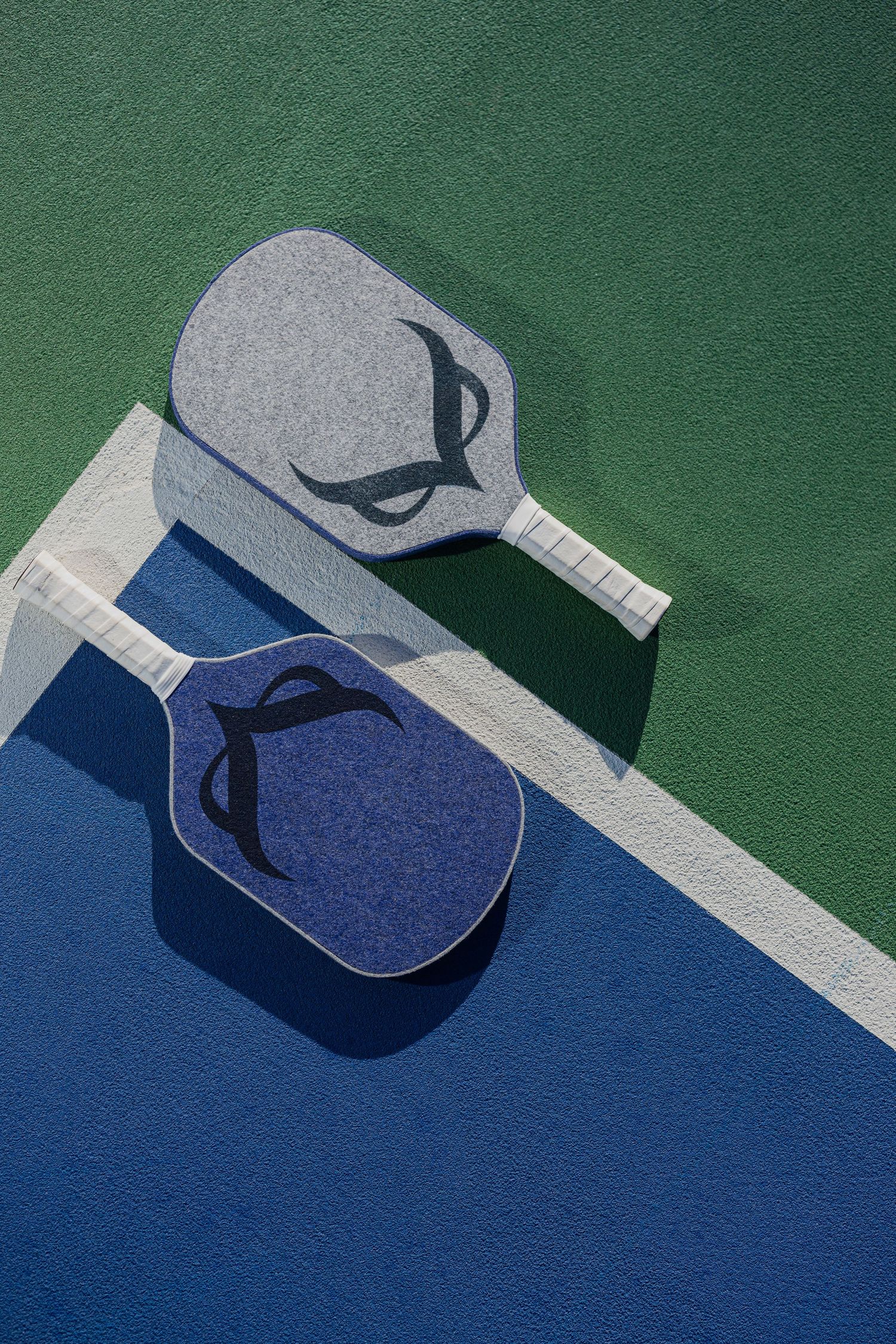 Grey and blue pickleball paddles arranged on a green and blue court surface.
