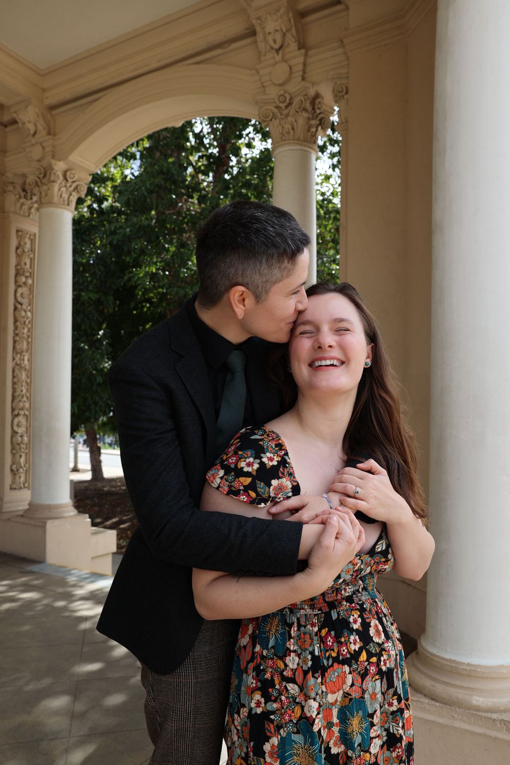 Couple embracing and laughing under ornate architectural columns.