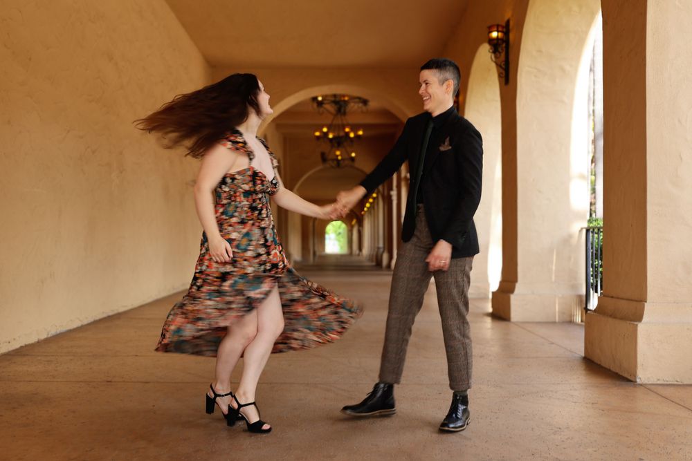 Couple dancing in covered outdoor hallway with floral dress twirling.