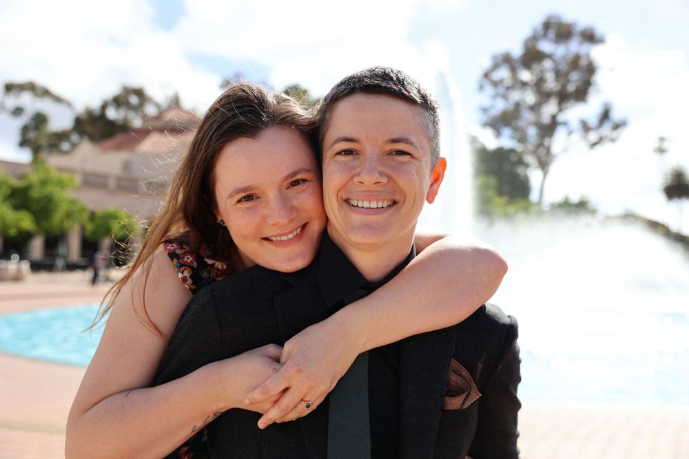 Couple sharing an embrace outdoors with bright sunlight and pool in background.