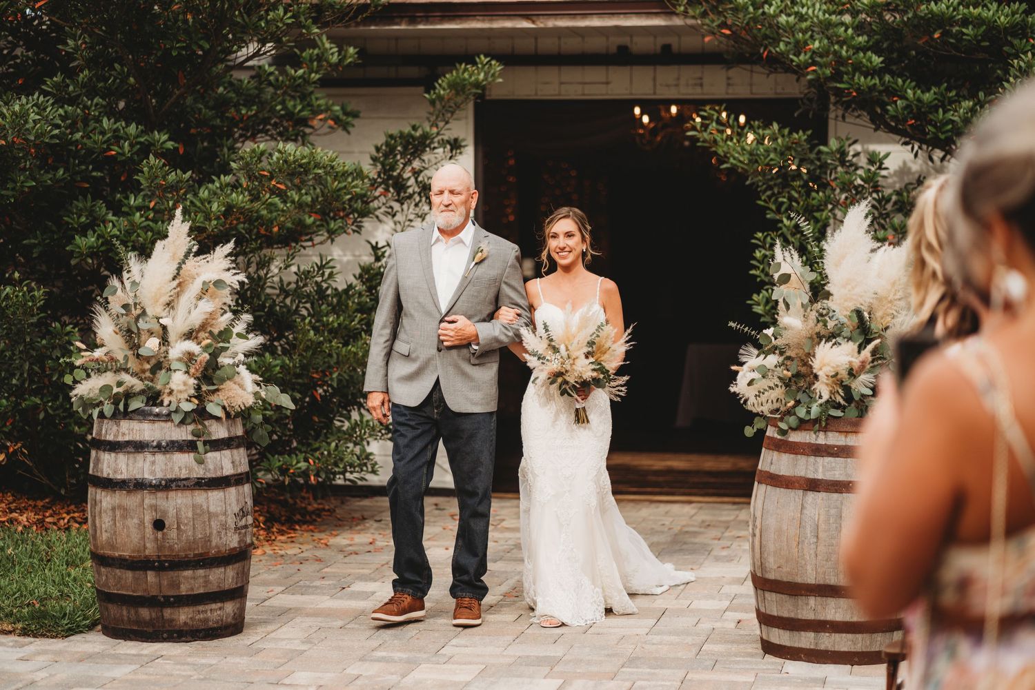 Bride and man walking out of rustic venue decorated with wine barrels and floral arrangements.