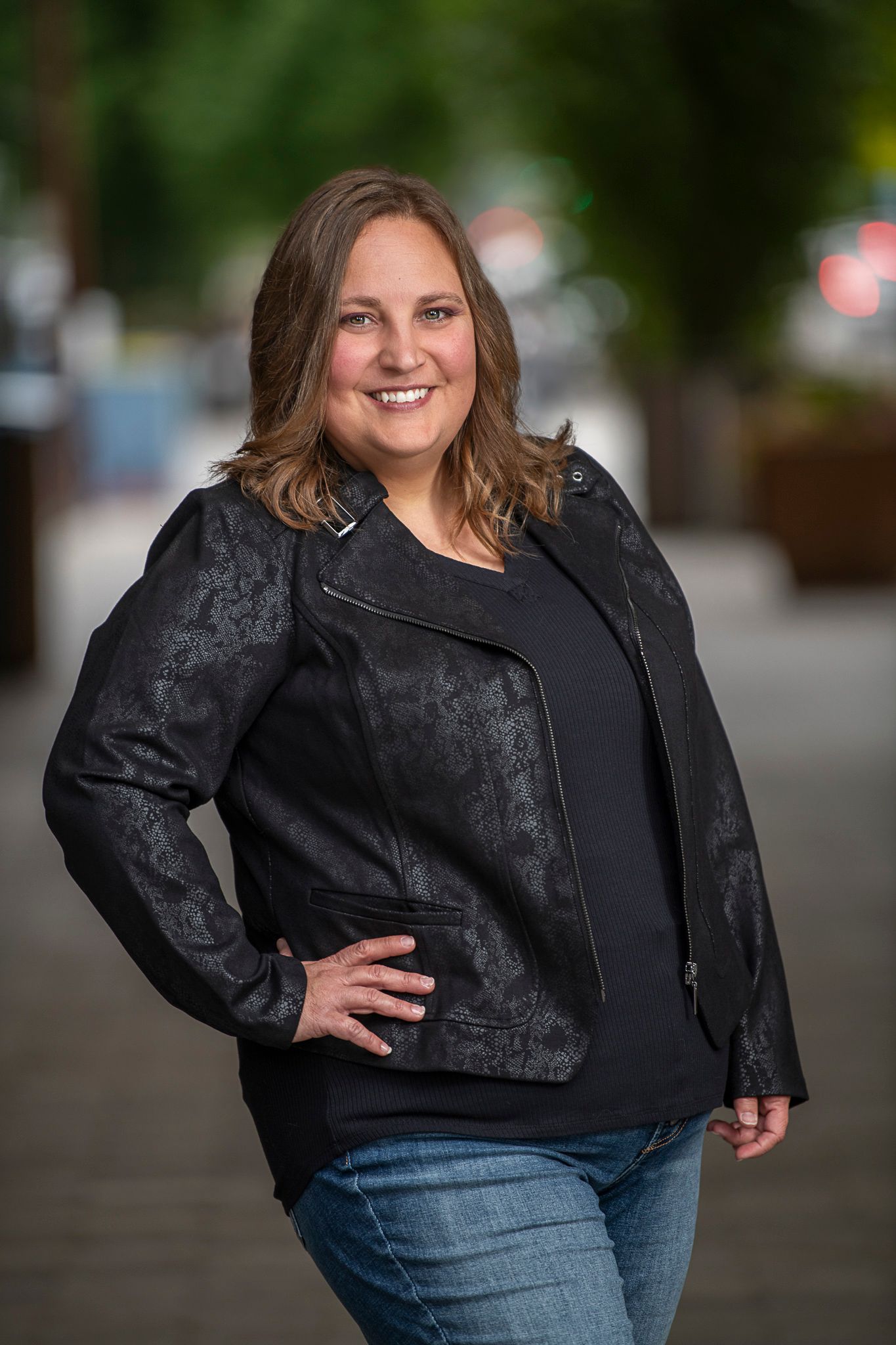 Person wearing black textured jacket standing confidently outdoors with blurred background.