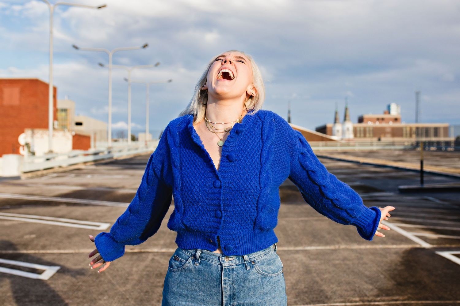 A joyful expression captured in an outdoor parking lot setting wearing a bright blue sweater.