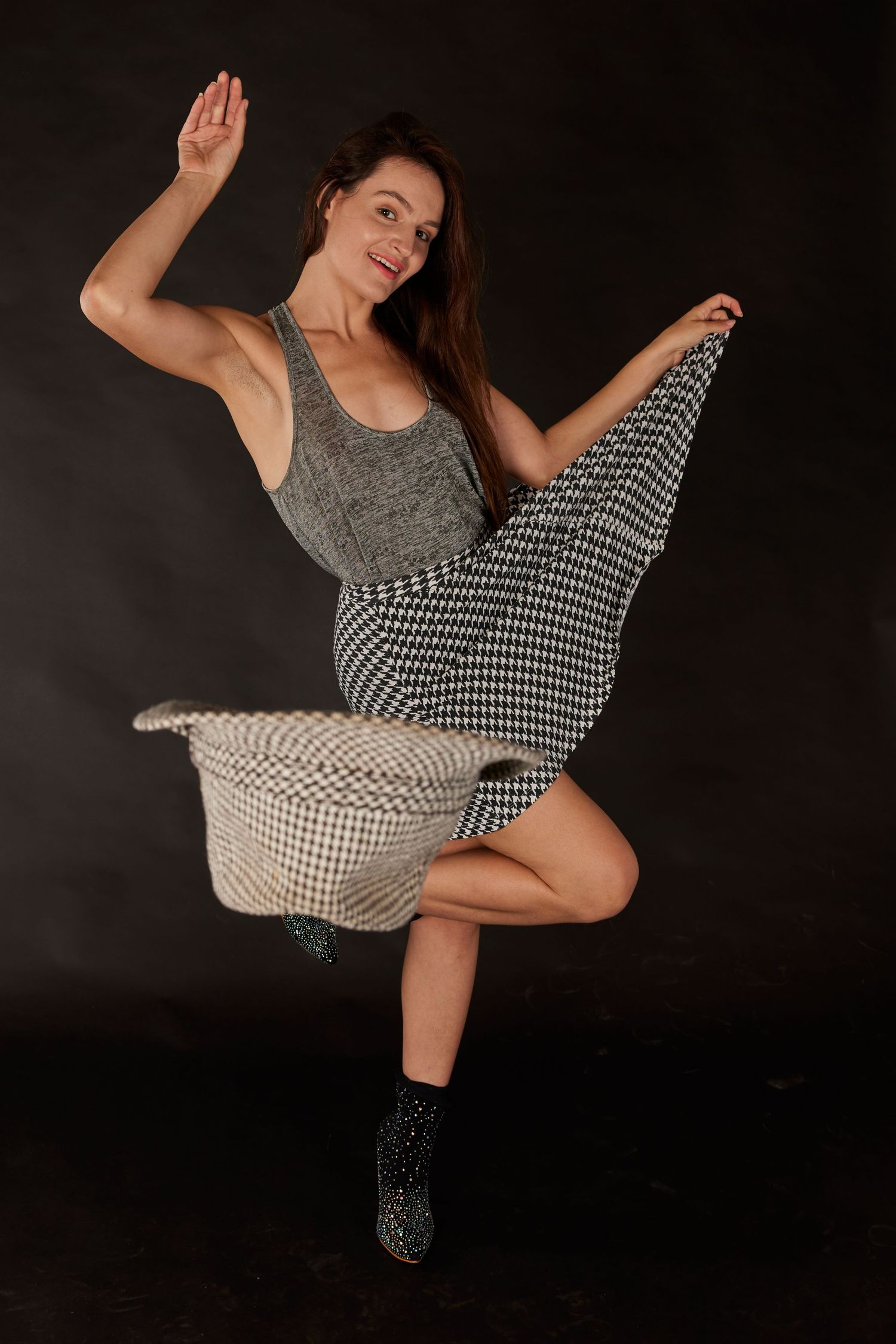Dancer in gray top and patterned skirt twirling against dark background.
