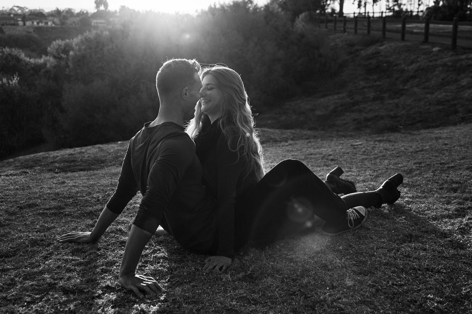 Silhouetted couple sitting on hillside during sunset in black and white photography.