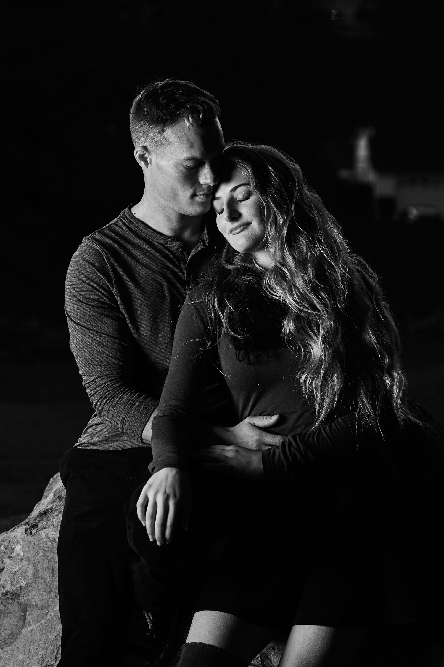 Intimate black and white portrait of couple sharing close moment in low light setting.