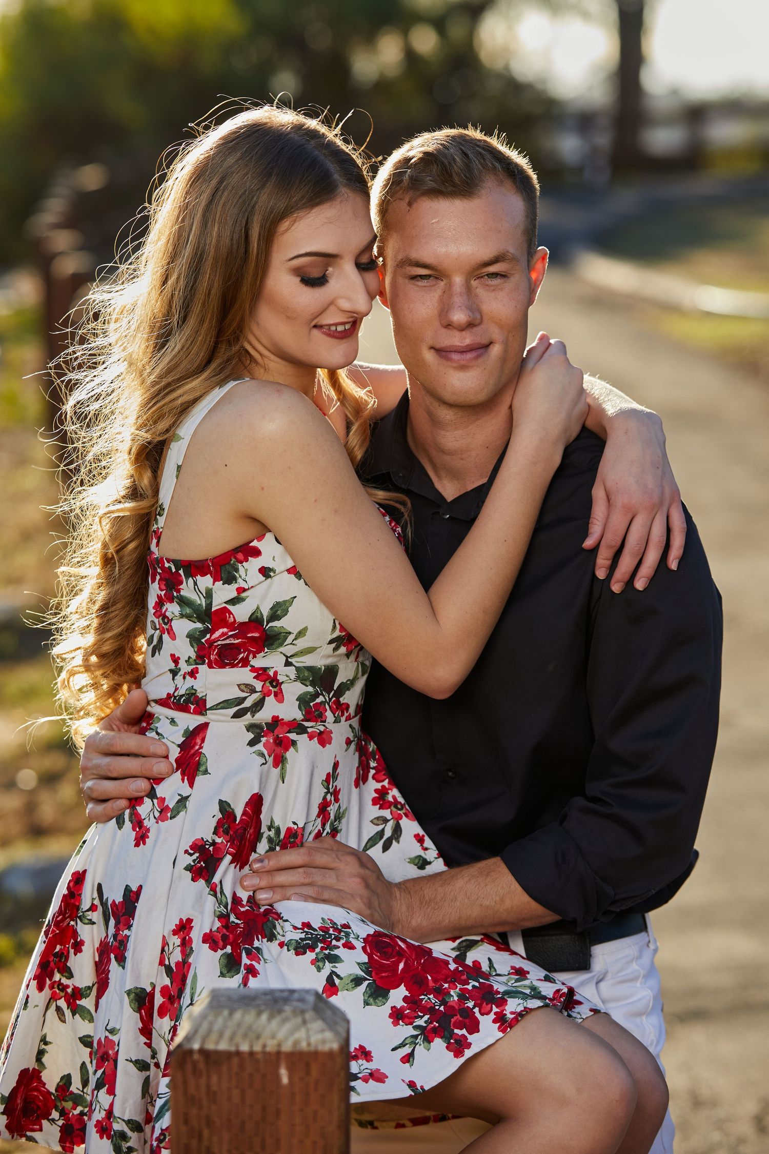 Romantic couple embracing outdoors with woman wearing floral dress during golden hour.