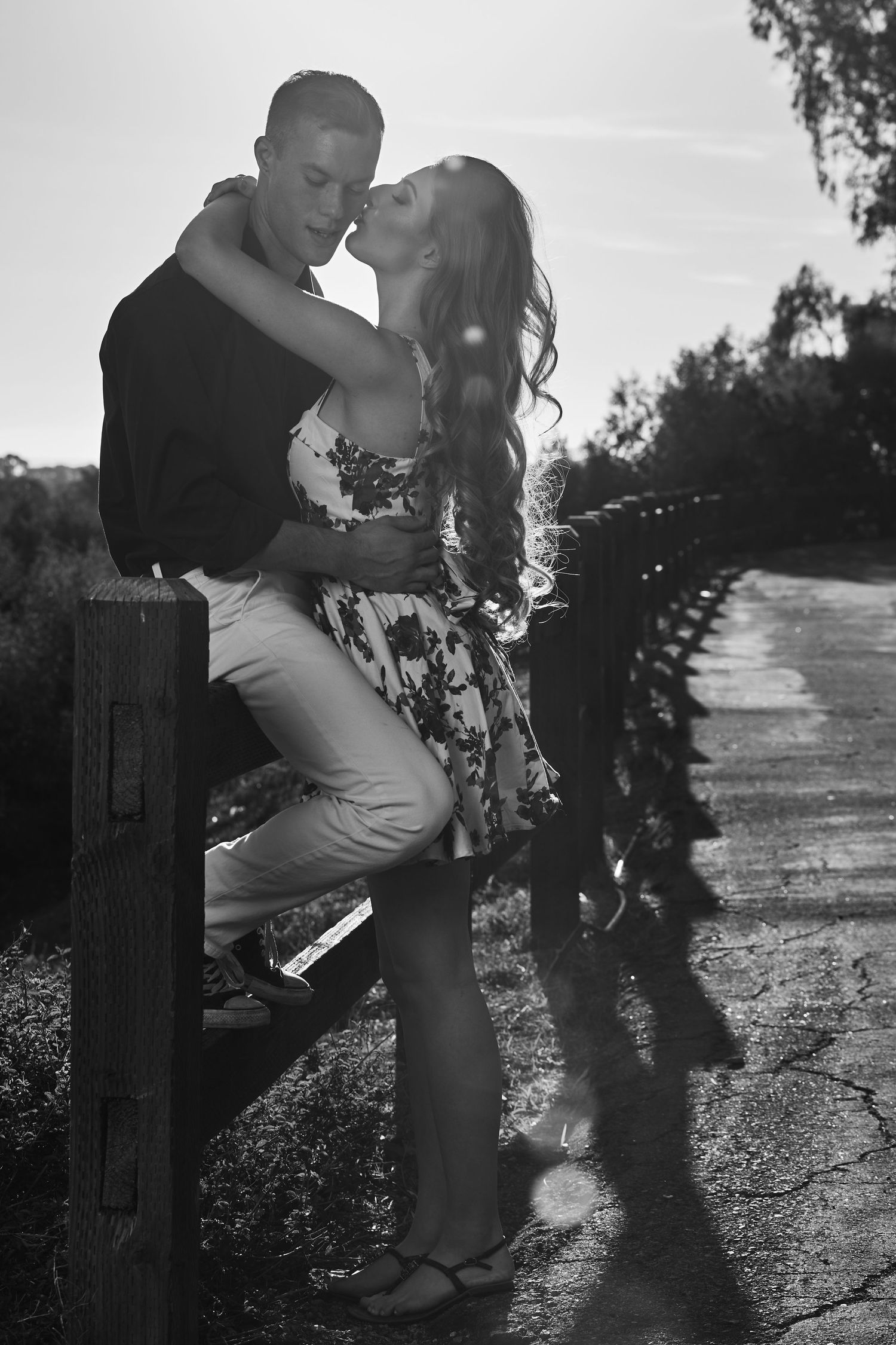Romantic black and white couple portrait along a fence at sunset.