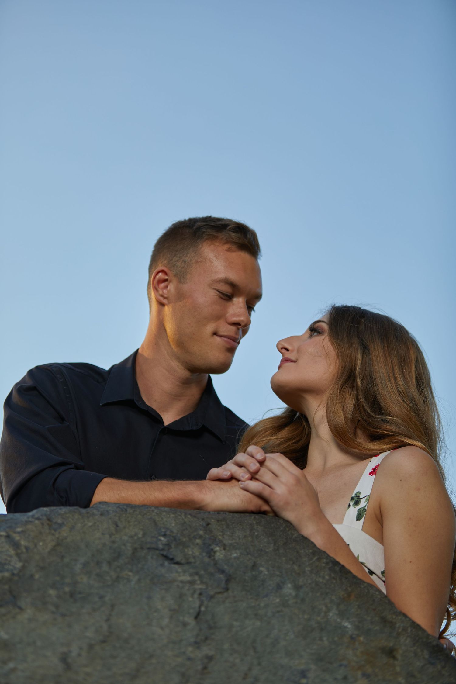 Intimate portrait of couple sharing tender moment against blue sky and rocky backdrop.