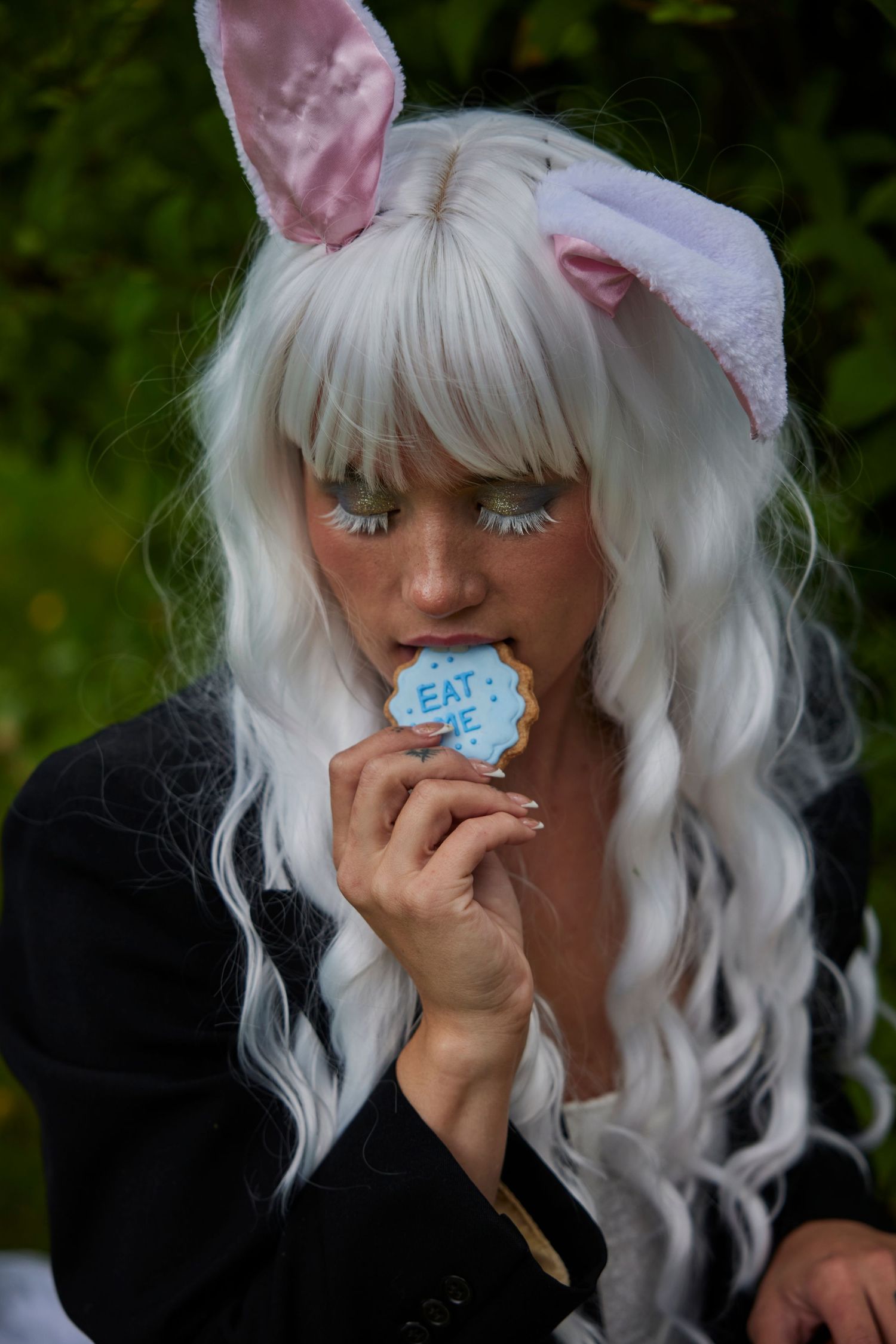 Cosplay look with white wig, bunny ears, and sparkly makeup biting into a treat.