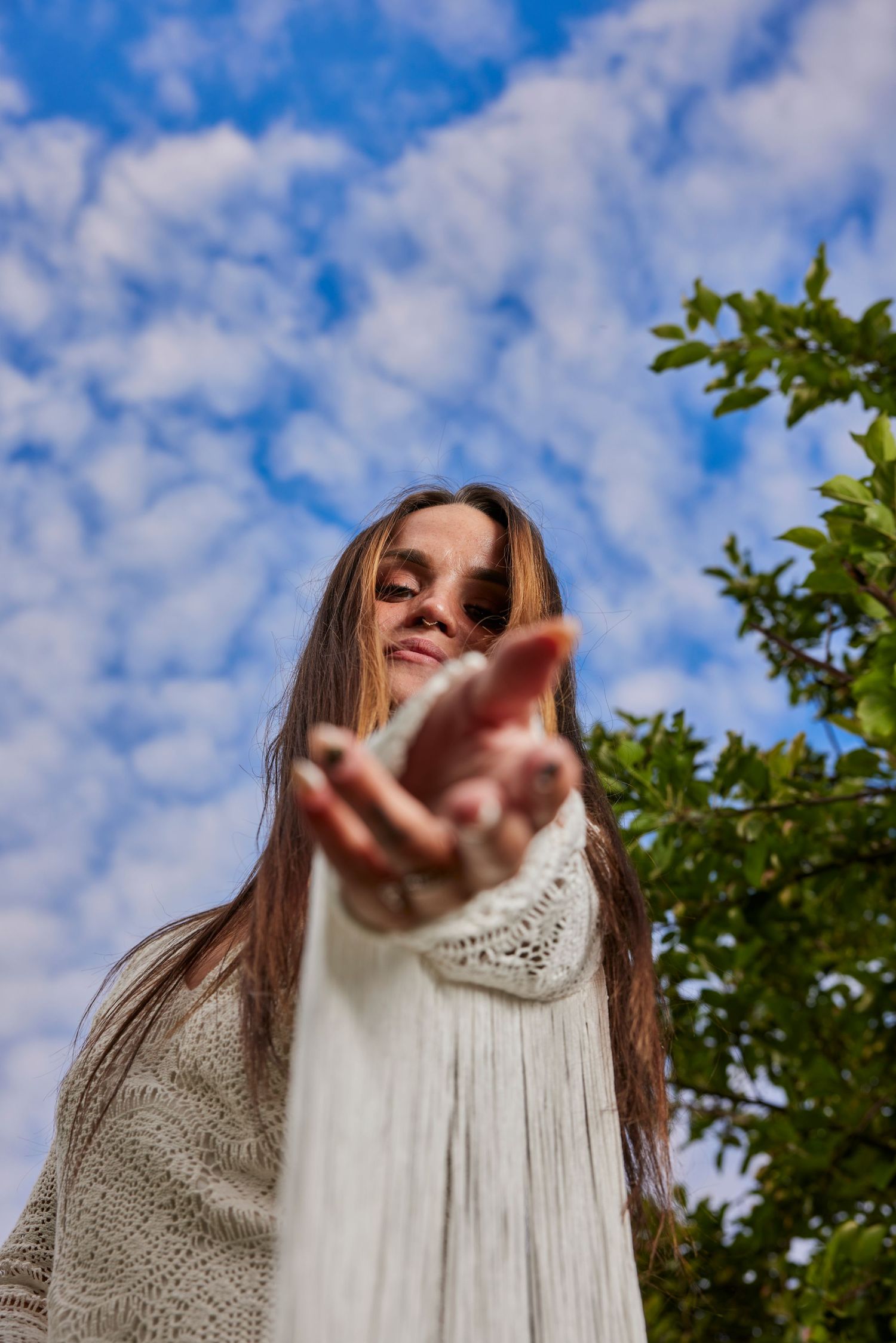 Low angle shot against blue sky and clouds with reaching hand in foreground.